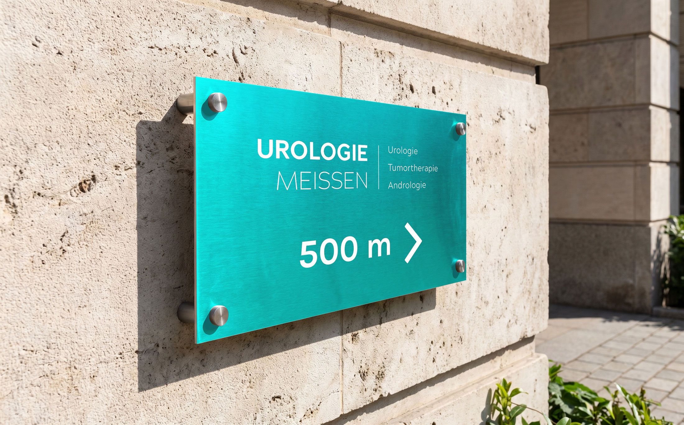 Wegweiser-Schild der Urologie Meissen in Türkis mit der Aufschrift „500 m“ an einer Natursteinfassade.